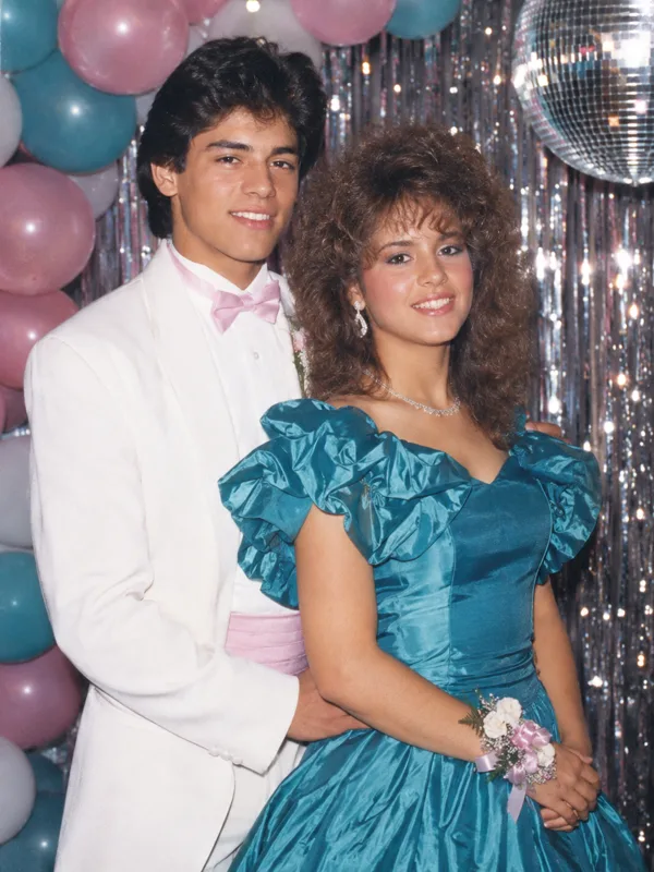 Teen couple in a white dinner jacket and teal taffeta gown at a 1980s prom balloon arch