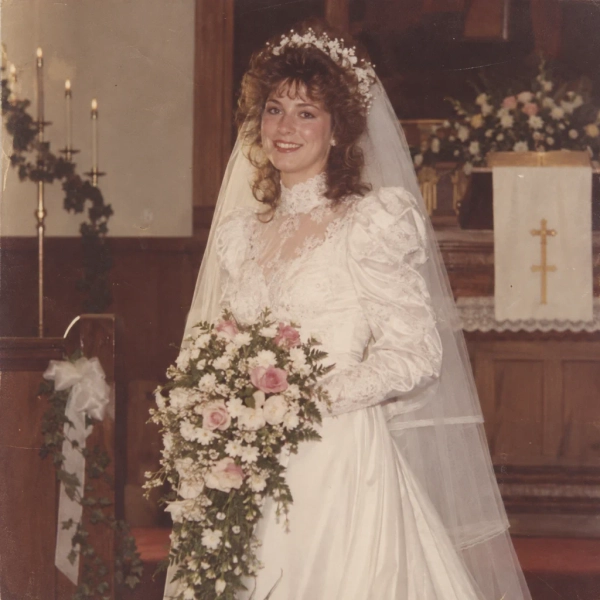 Bride in a puff-sleeved lace gown holding a cascade bouquet at a 1980s church altar